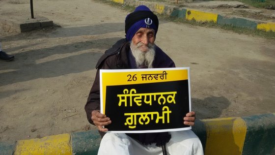 An elderly Sikh man holds a placard